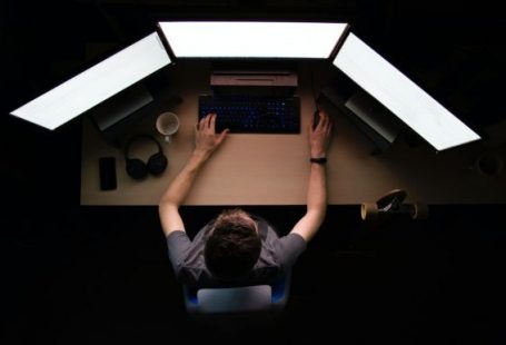 Programming - man facing three computer monitors while sitting