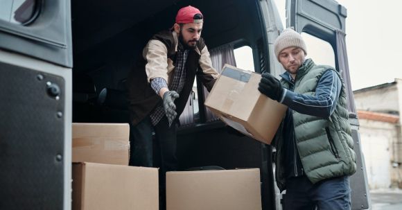 Continuous Delivery - Man in Black Jacket and Red Knit Cap Holding Brown Cardboard Box